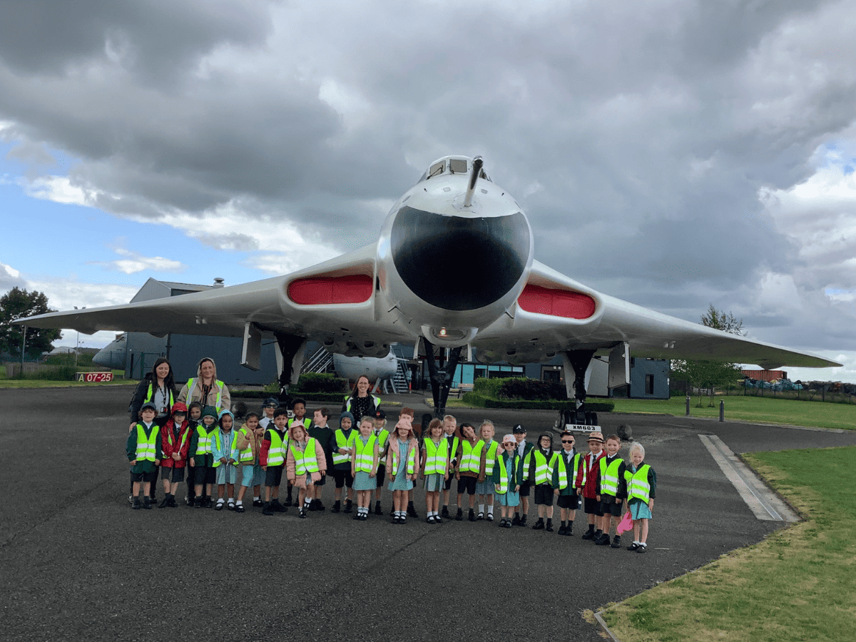 Woodford Primary School pupils from Reception stand in front of a plane at Avro Heritage Museum