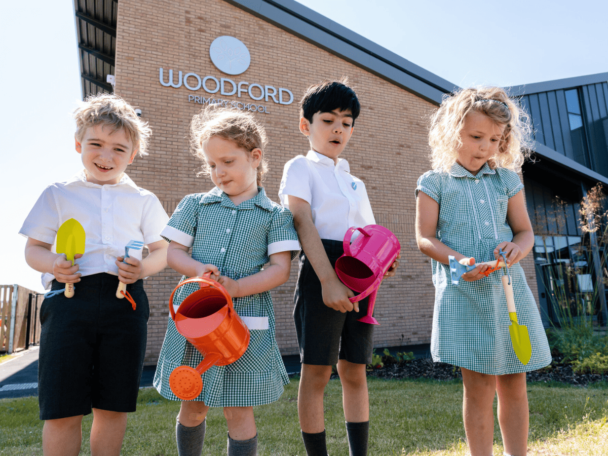 Woodford Primary School pupils hold gardening tools donated by Redrow.